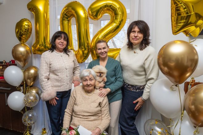 Priekšplānā – jubilāre Marija Siļicka. No kreisās: Jūrmalas domes Kultūras, tūrisma un kurortoloģijas komitejas priekšsēdētāja Ligita Maziņa, jubilāres mazmeita Karina ar jubilāres sunīti rokās un Labklājības pārvaldes vadītāja Laima Grobiņa. Foto - www.jurmala.lv