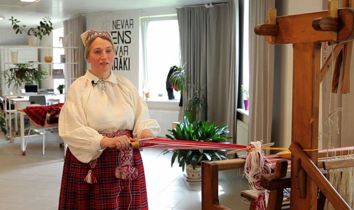 Lielvārdes tautastērpa pētniece un audēja Edīte Kuzmane ne vien pati ir čakla audēja, bet savas prasmes nodod arī skolēniem. Foto – ekrānuzņēmums no video